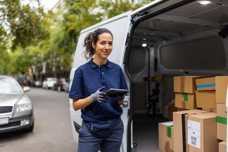 Female courier worker standing by delivery van