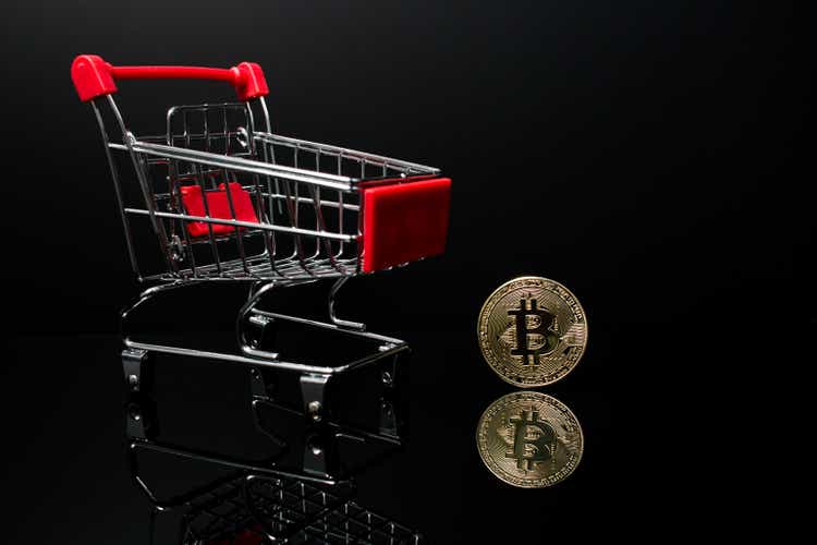 A shopping cart with a crypto currency Bitcoin coin next to it with a black background.