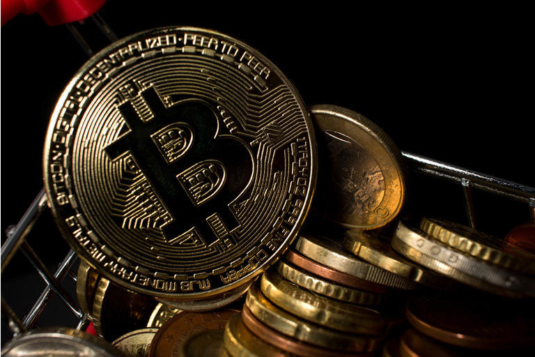 Closeup of bitcoin coin in a shopping cart with euro coins. BTC coin with dark background.