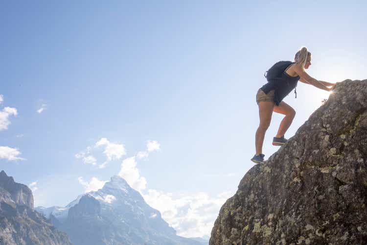 Young woman scrambles up mountain ridge at sunrise