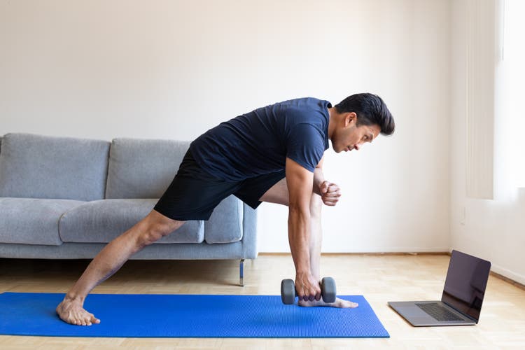 Man watching online video and doing dumbbell exercises at home