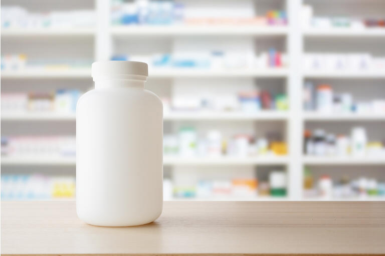 White medicine bottle on wood counter with pharmacy drugstore shelves blur pharmaceutical background