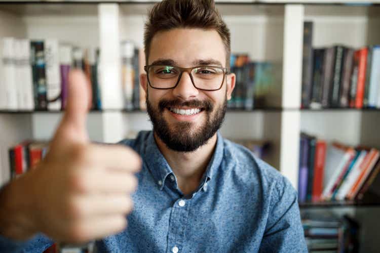 Camera point of view of young man holding thumbs up at home office