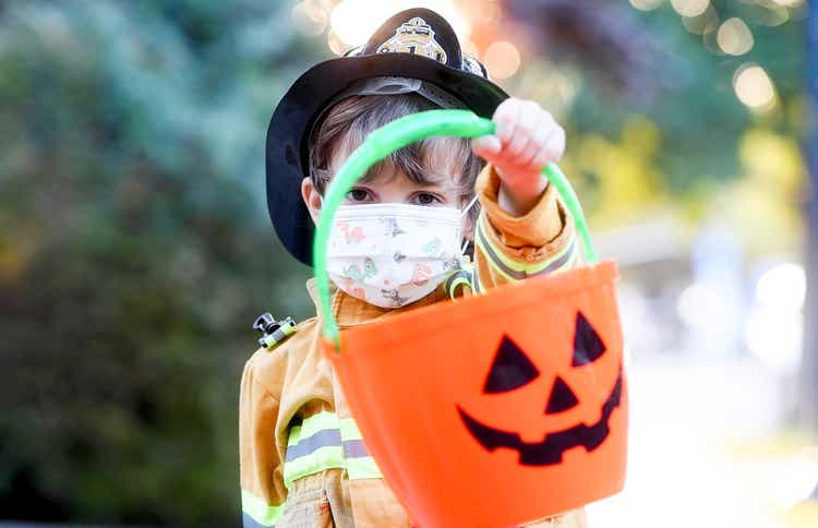 Serious little boy wearing a halloween fireman costume and a protective face mask looking at the camera holding a Jack o Lantern bucket