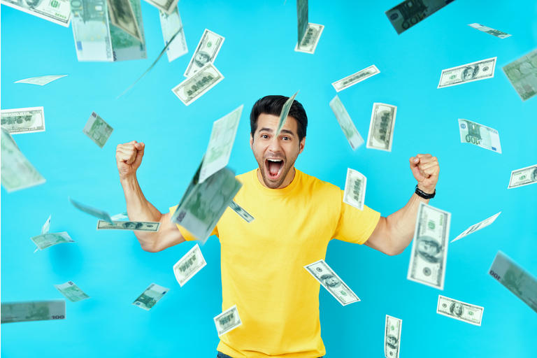 Happy excited man standing under money rain banknotes falling down