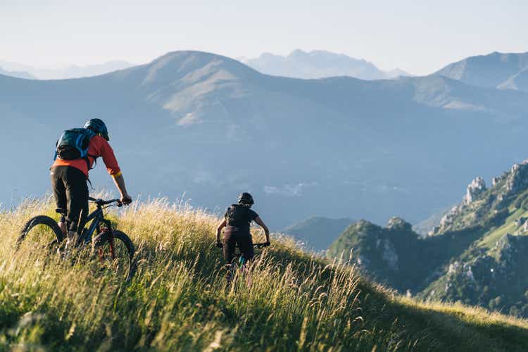 Mountain bikers ride down grassy mountain ridge