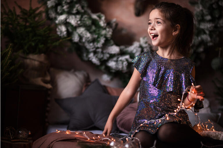 Excited girl in pretty dress playing with Christmas lights