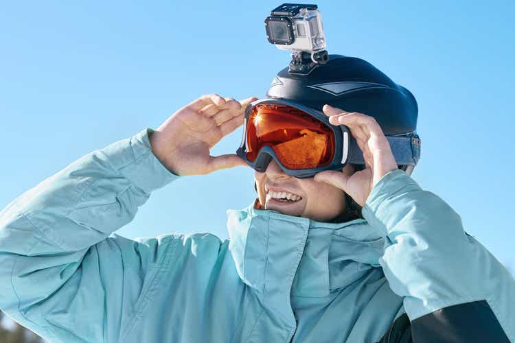Skier with action camera on a helmet. Ski goggles with the reflection of snowed mountains. Portrait of man at the ski resort on the background of mountains and blue sky,. Wearing ski glasses