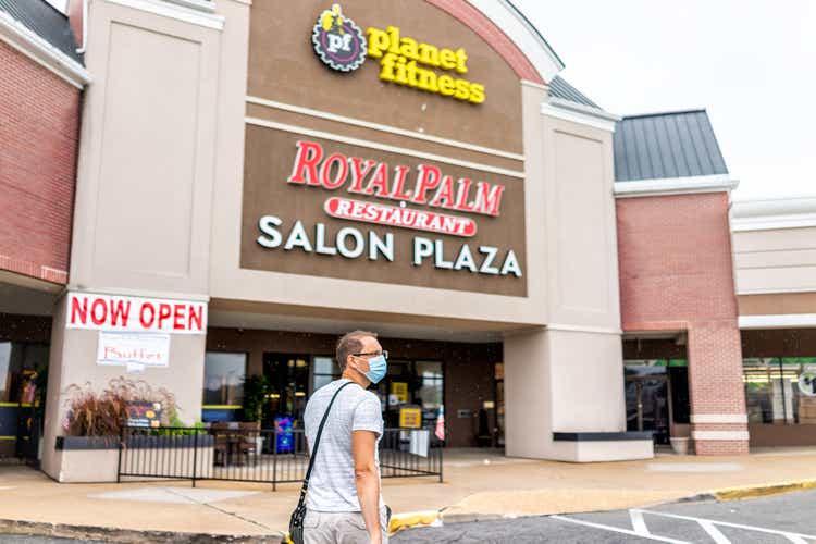 Strip mall plaza with man in mask walking towards planet fitness sign and now open during Covid-19