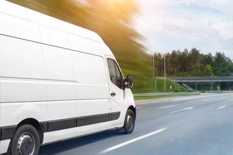 Weiße moderne Lieferung kleine Lieferung Fracht Kurier Van bewegt sich schnell auf autobahnstraße in die Stadt Vorort. Busines Distribution und Logistik Express-Service. Minibus fährt an sonnigem Tag auf der Autobahn