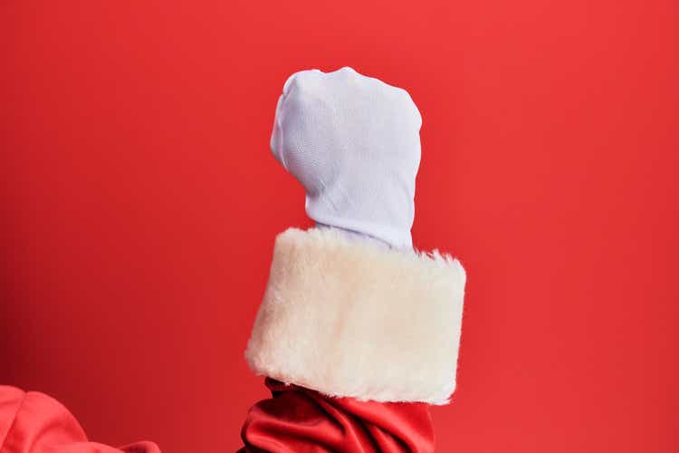 Hand of a man wearing santa claus costume and gloves over red background doing protest and revolution gesture, fist expressing force and power