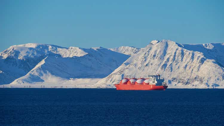 Big red painted LNG (liquefied natural gas) carrier vessel lying at anchor in the arctic ocean in front of Sørøya island with snow-covered mountains near Hammerfest, Norway in winter.