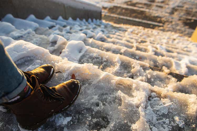 Danger of slipping. Female boots on rough slipper ice surface. A woman in brown leather shoes descends the slippery ice ladder