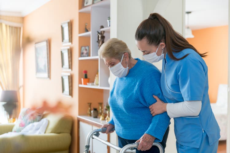 Home caregiver wearing a facemask while assisting a senior woman walking with a mobility walker