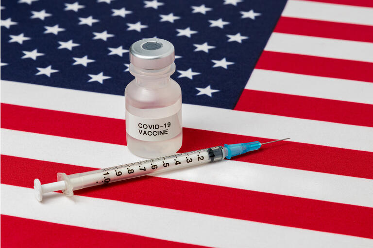 Closeup of vial with Covid-19 vaccine, syringe and needle on United States of America flag. Concept of medical research and treatment, coronavirus pandemic and healthcare.