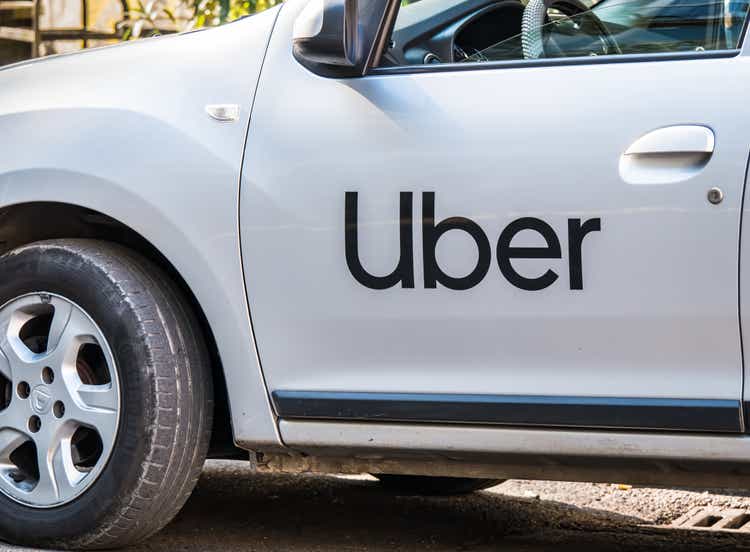 Uber logo inscriptioned on a white painted car. Uber car in traffic.