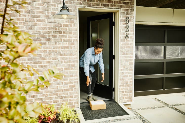 Smiling woman picking up package from front porch of home