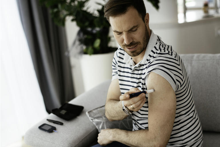 Young man giving himself an insulin shot at home. stock photo