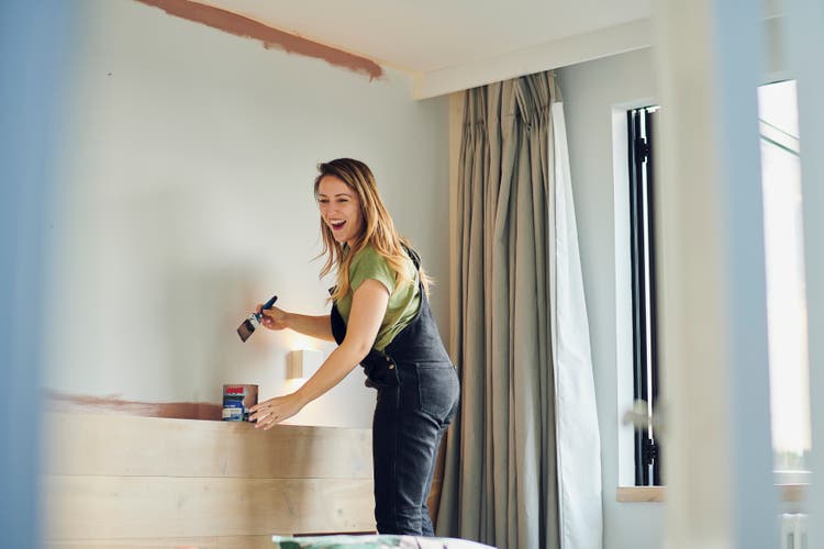 Young Woman laughs whilst painting bedroom wall