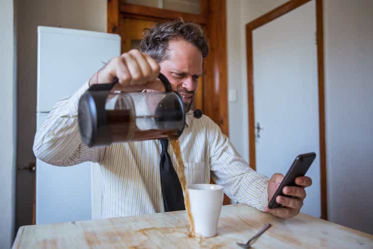 Man looking at his mobile phone spills coffee all over the table while at work