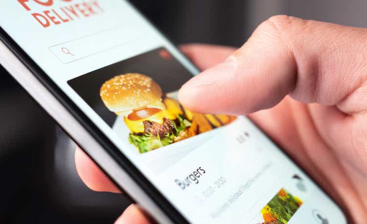 Food delivery app order with phone. Online mobile service for take away burger and pizza. Hungry man reading restaurant menu, website and reviews with smartphone.