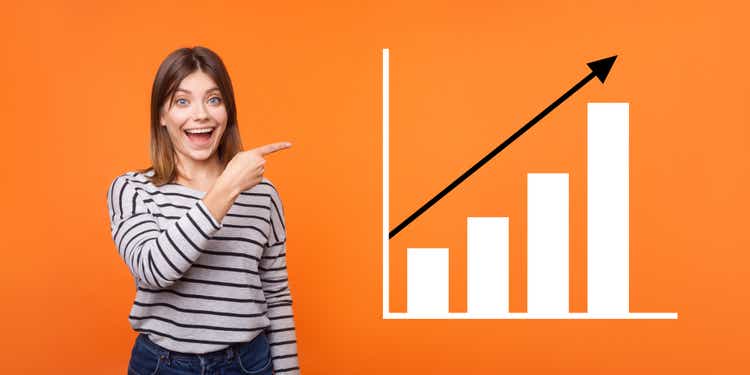 Portrait of amazed happy joyful young woman standing, pointing aside and showing business growth graph.