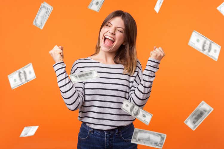 Money rain. Yes I did it! Portrait of joyous winner, young woman in casual shirt standing with clenched fists and closed eyes, celebrating victory and richness.