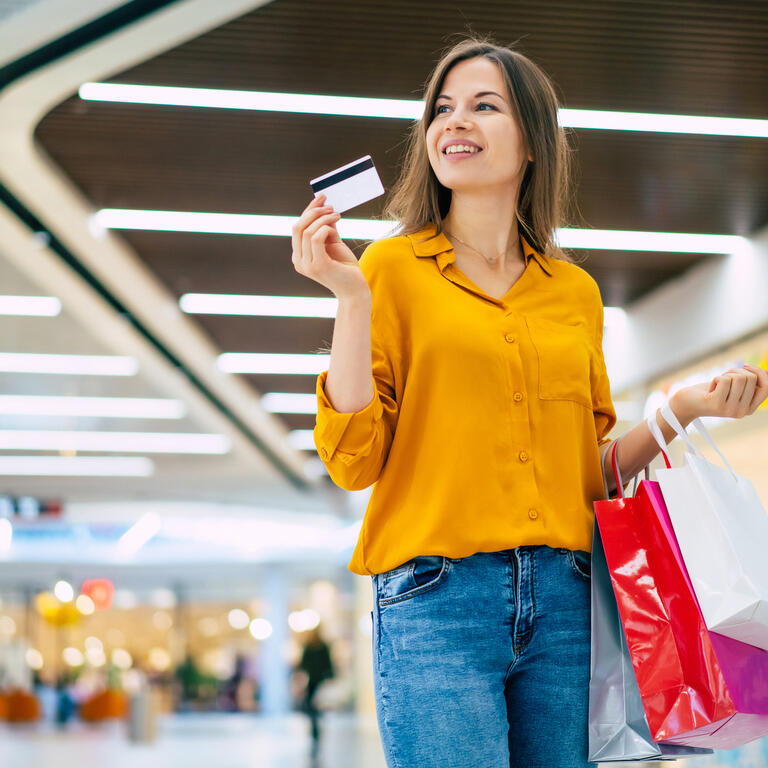 Excited gorgeous smiling young woman is posing with a credit card and shopping bags in the mall
