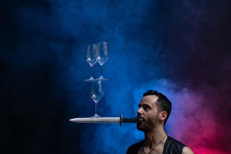 Man hold knife in the mouth and keep in balance wineglasses on it. concentration