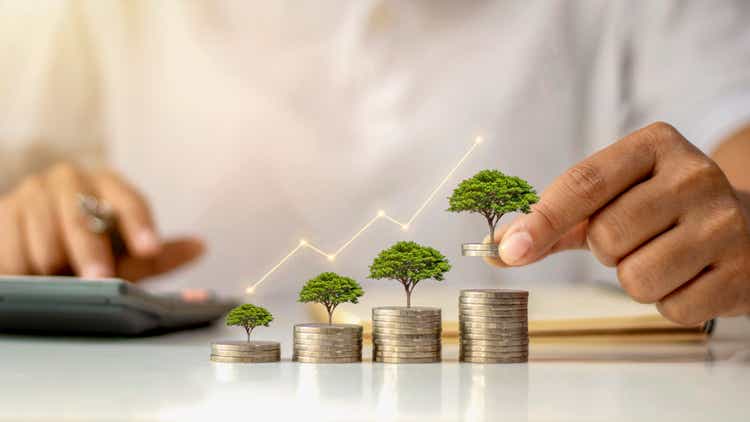 A businessman holding a coin with a tree that grows and a tree that grows on a pile of money. The idea of maximizing the profit from the business investment.