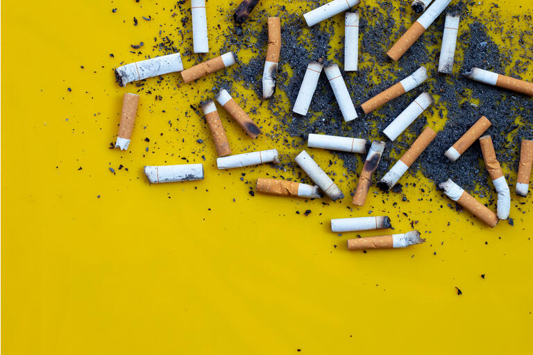 Cigarette butts and ash on yellow background.