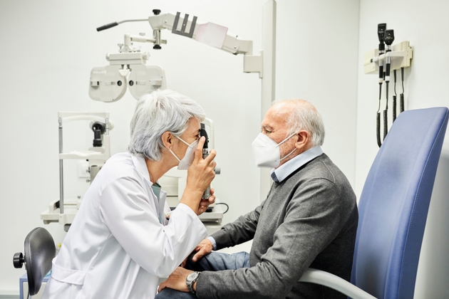 Doctor examining aged man through eye equipment
