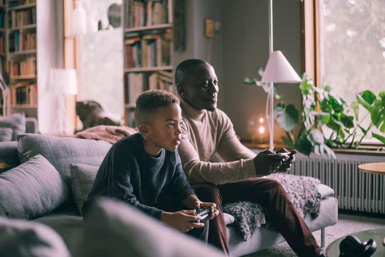 Père et fils souriants jouant à un jeu vidéo assis sur un canapé à la maison