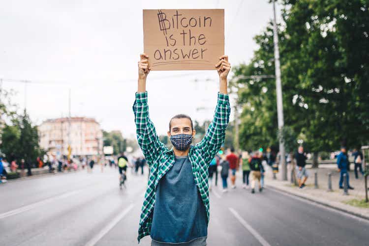 Young man with a face mask and a poster in his hands about Bitcoin. Young activist / protester. Blockchain activist