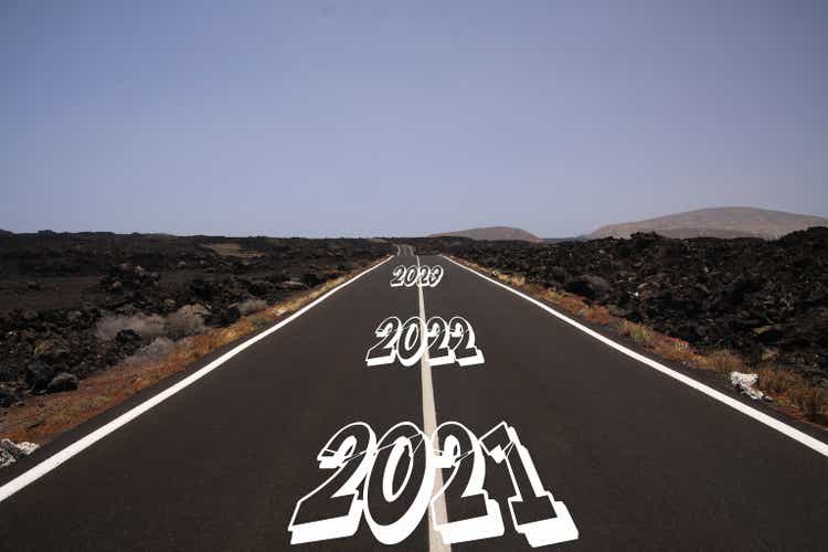 Long hard stony successful way concept: view on endless asphalt road through dry arid volcanic landscape with numbers of years 2021, 2022, 2023