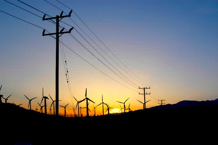 Windmill farm in the desert of Palm Springs, California at sunset with power lines leading to the city.