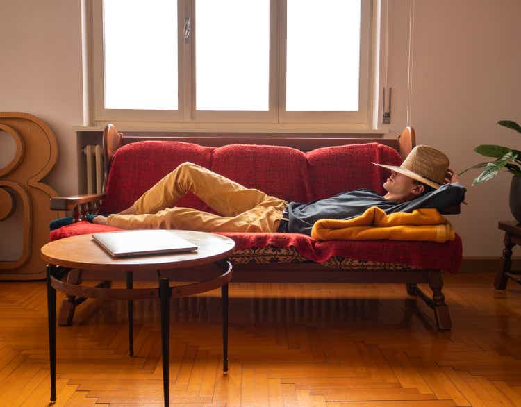 Young man wearing a hat sleeping on the sofa waiting for inspiration, lazy boy rests during break to recharge his energy