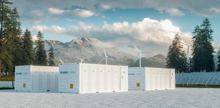 Modern container battery energy storage power plant system accompanied with solar panels and wind turbine system situated in nature with Mount St. Helens in background. 3d rendering.