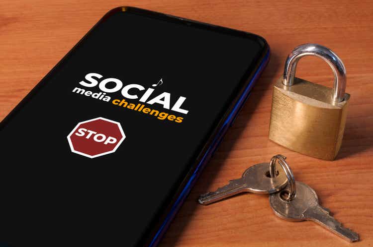 Smartphone showing the message "stop social media challenges" a wooden table with a lock and keys.