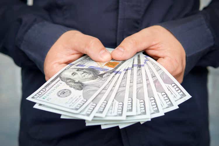 male hands with wrist watch is considered American dollars. Hands holding dollar cash. 1000 dollars in 100 bills in a man hand close-up on a dark background. hundred