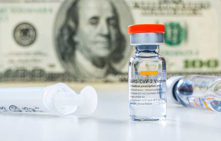 Covid-19 vaccine ampoules and syringe with 100 US dollar banknote on the background