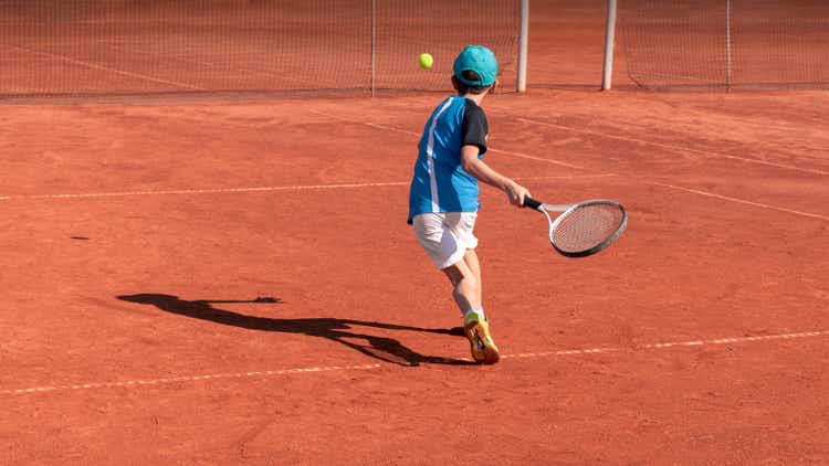 Child on tennis court. Boy tennis player learning to hit forehand . Physical activity and sports education of children. Tennis training at school or club. Background, copy space