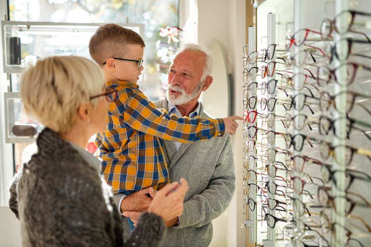 miling grandparent choosing the most suitable eyeglasses at optician store