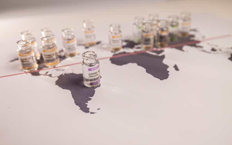 Image of a world globe map with vials for the global SARS/COVID pandemic vaccine war, with vaccine hoarding, restricting equal access to vaccines across the world, counteracted by the Covax programme and global vaccine alliance