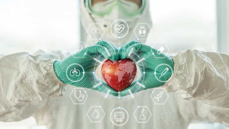 Medical technology, global health tech and world heart health day concept with cardiologist doctor in ppe for covid-19 protection holding heart in hospital cardiac lab for laboratory science research