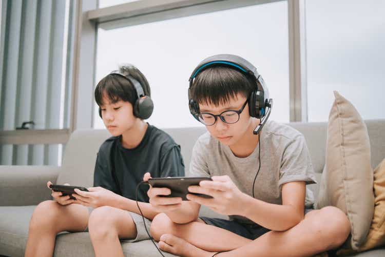 asian chinese brother playing multiplayer online gaming with headset in living room using smart phone connection