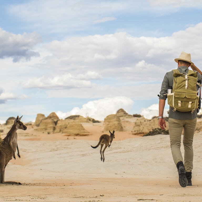 Young man walking in arid desert landscape with photography backpack on an adventure in outback Australia