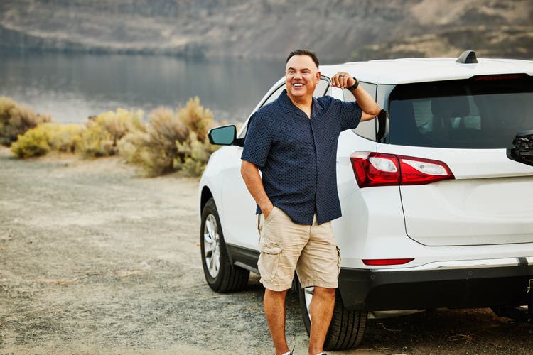 Smiling mature man standing next to car during road trip