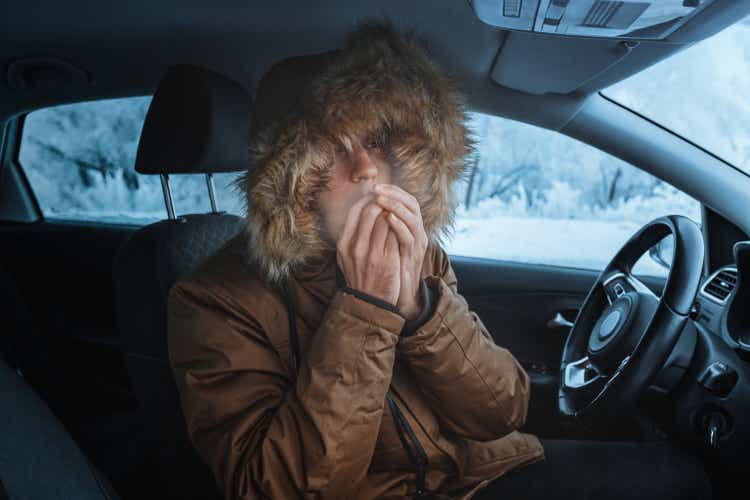 Мужчина в куртке старается согреться и не замерзать в заглохшем зимой автомобиле. Концепция опасной аварии или отказа обогревателя в холод