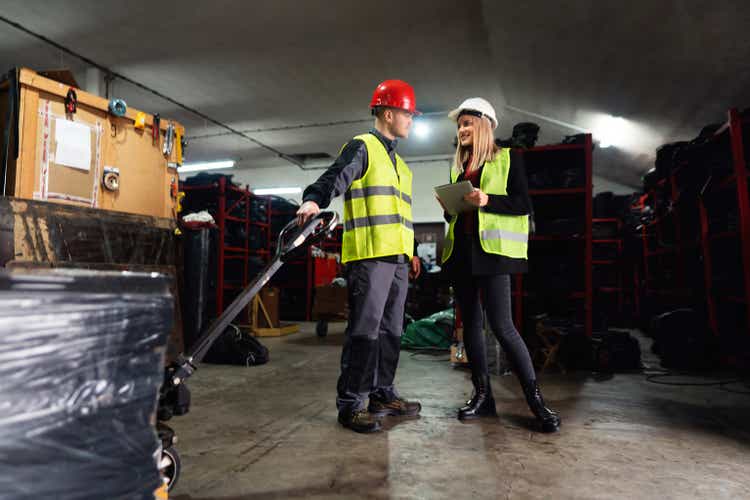 Young male worker and warehouse manager sorting finished rubber mats for the gym in a warehouse by using a digital tablet and pallet jack